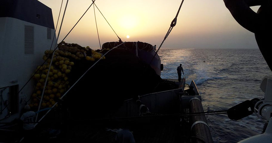 Echebastar fishery ship with sunset Silhouette of fishing gear and man on deck of large ship at sea facing setting sun